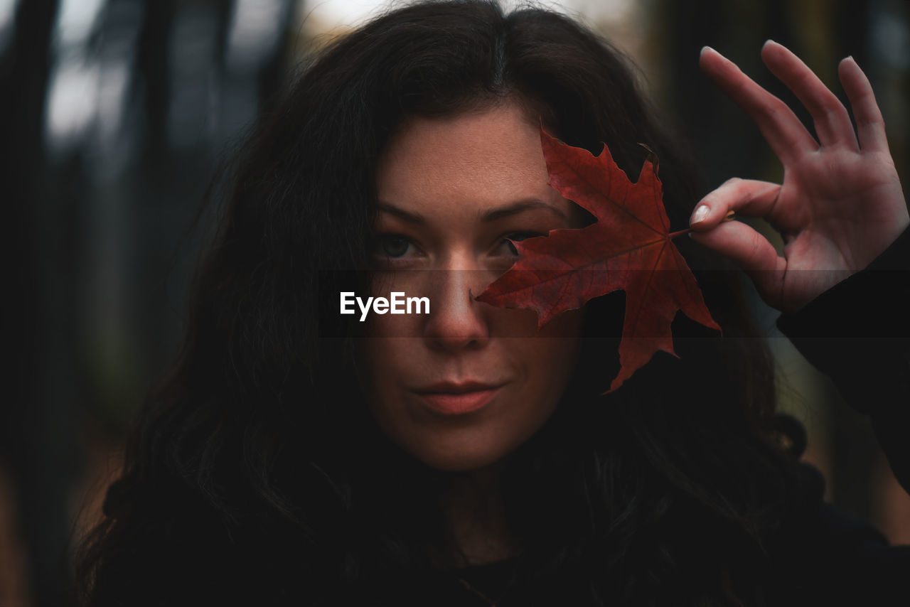 Close-up portrait of a beautiful young woman with leave against eye 