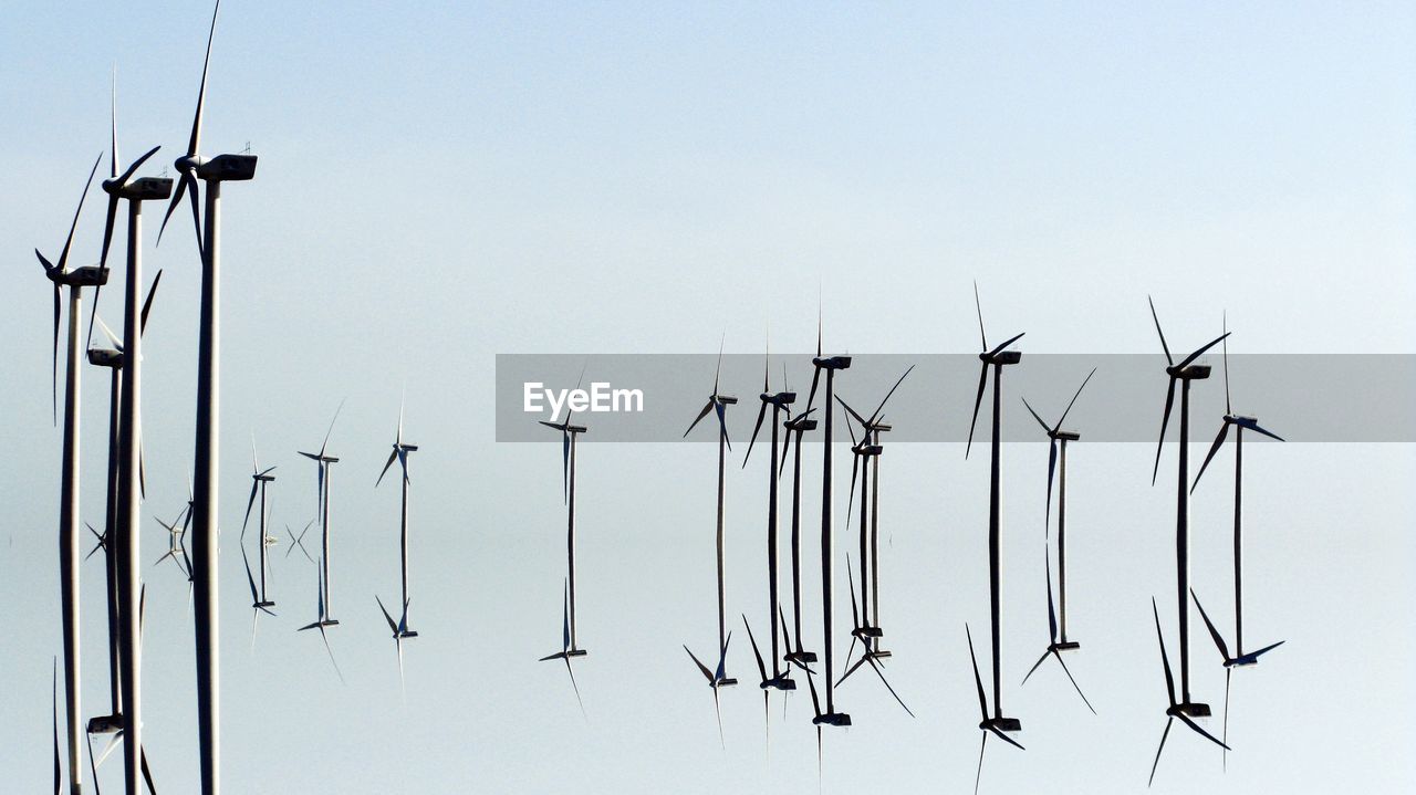 Reflection of windmills in sea against sky on sunny day