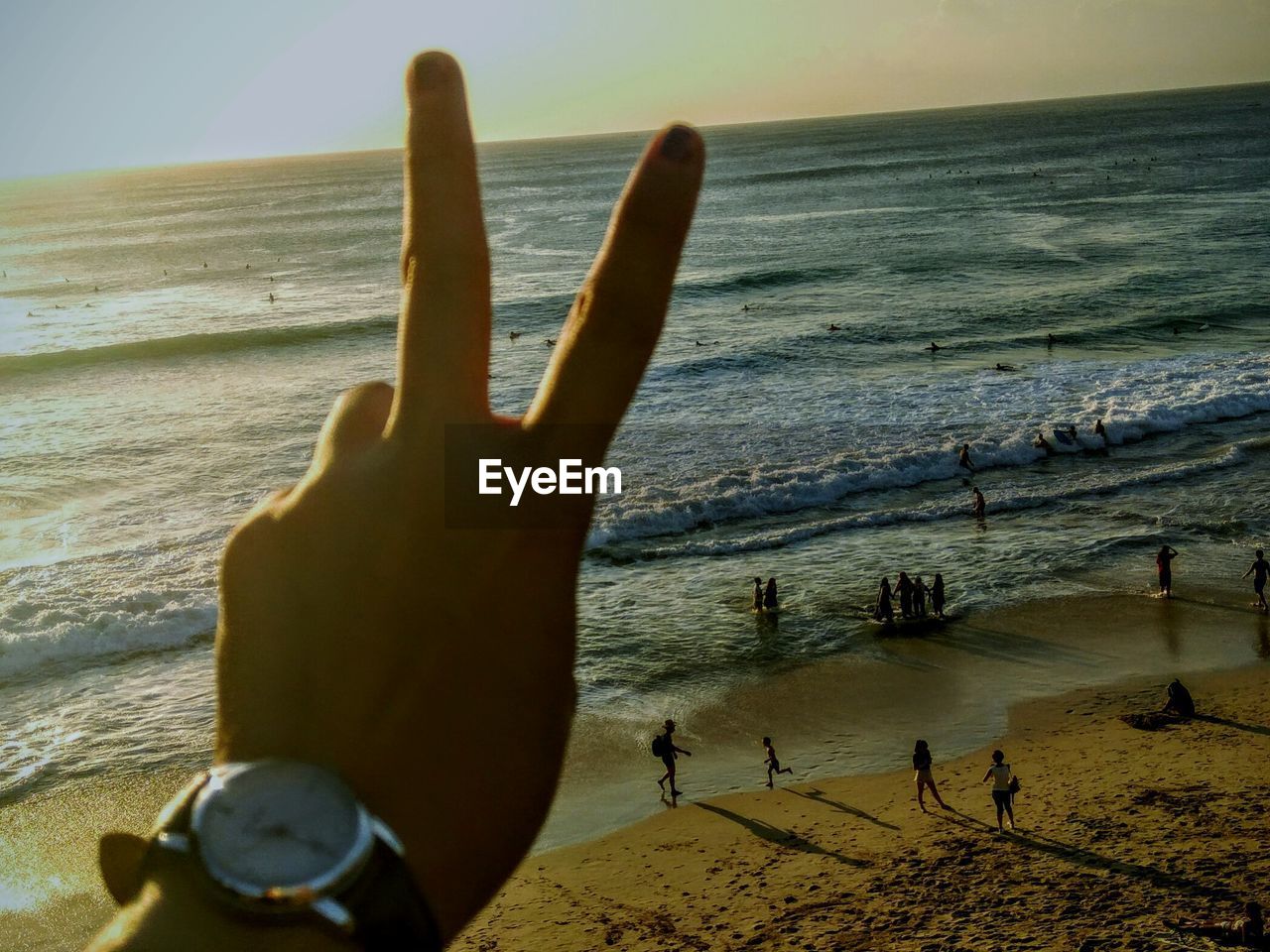 Cropped hand of man gesturing peace sign at beach