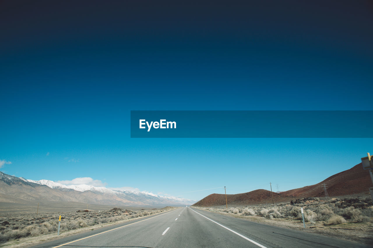 Road passing through landscape against clear blue sky