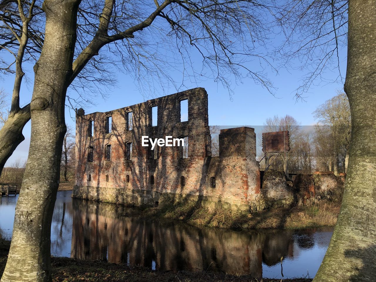 tree, architecture, reflection, plant, water, nature, bare tree, sky, built structure, history, no people, the past, ruins, day, building exterior, branch, autumn, old ruin, outdoors, waterway, building, urban area, lake, travel destinations, clear sky, old, château, tranquility