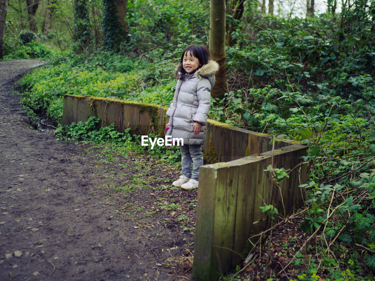 Full length of smiling young girl standing in forest park 