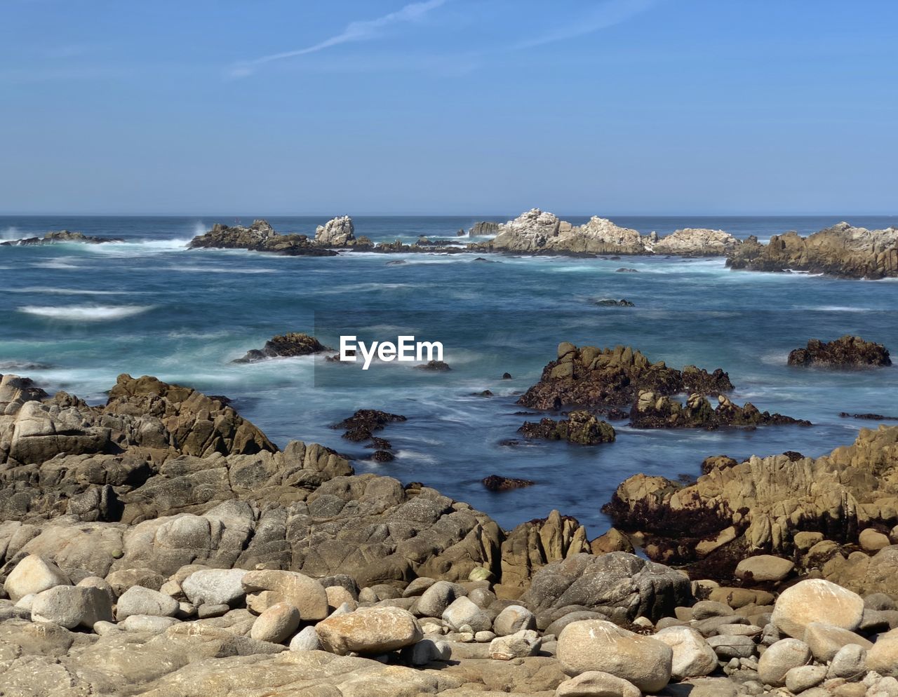 Rocky coastline of pacific grove, california with blue sky and slow shutter
