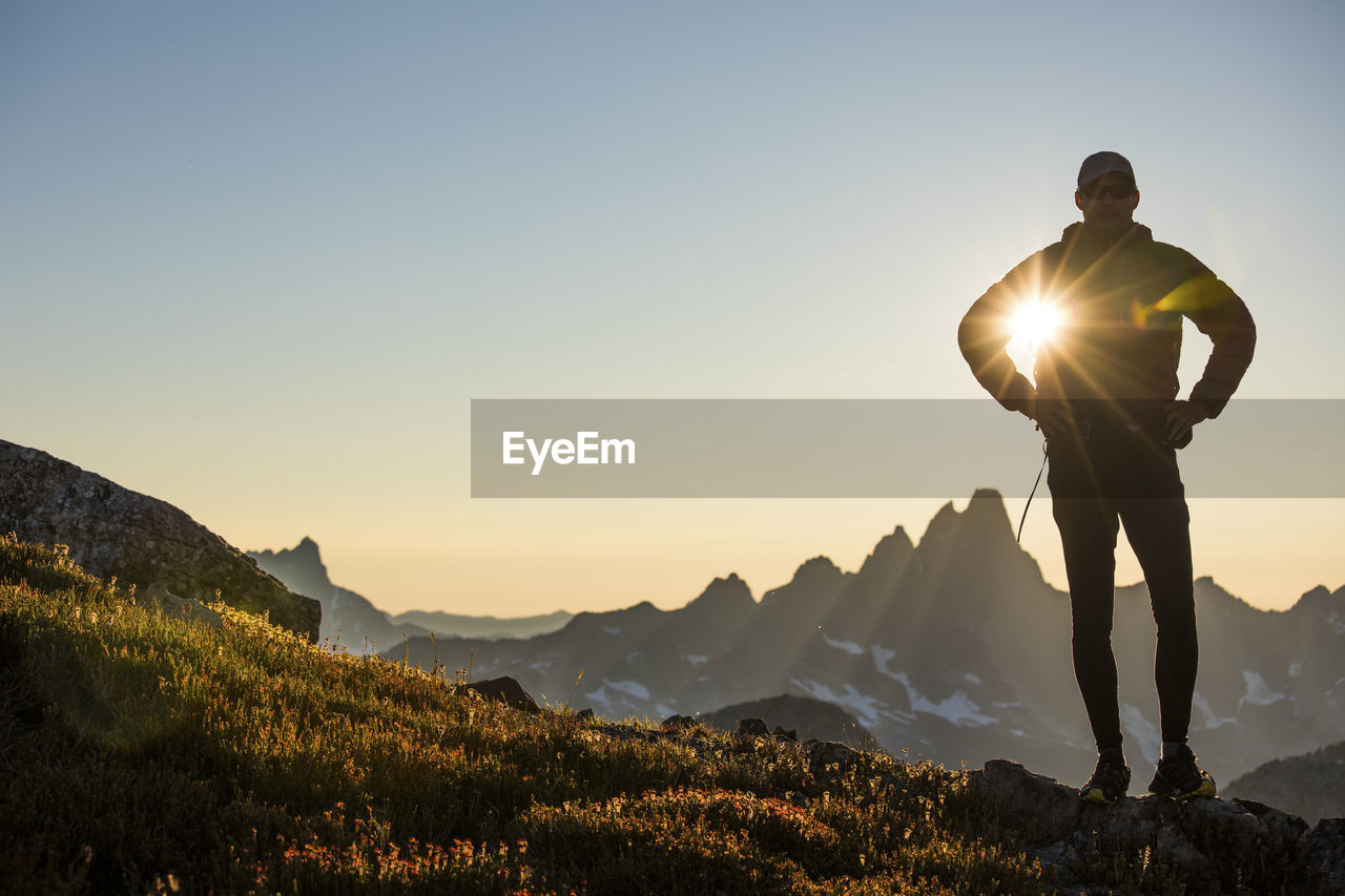 Sun shines through arm of silhouetted hiker on mountain ridge