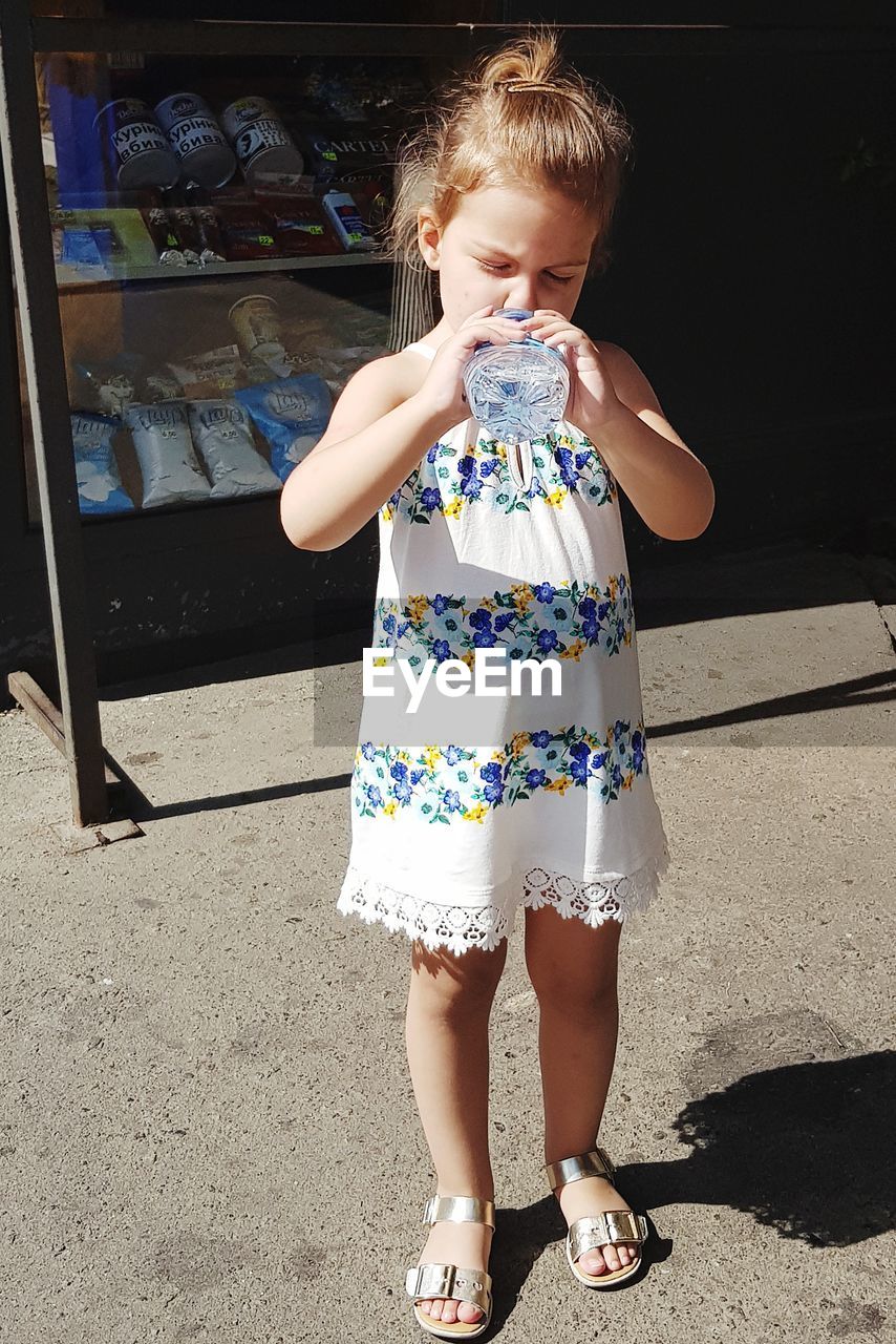 Cute girl drinking water from bottle on footpath