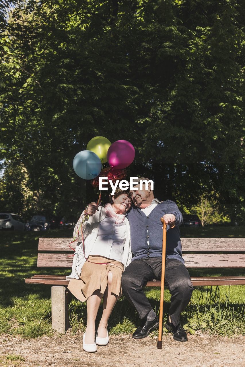 Happy senior couple with balloons sitting on bench in a park