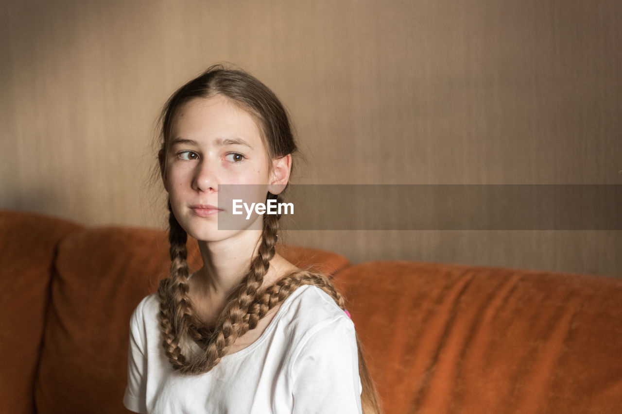 Teenager girl looking away while sitting on sofa at home