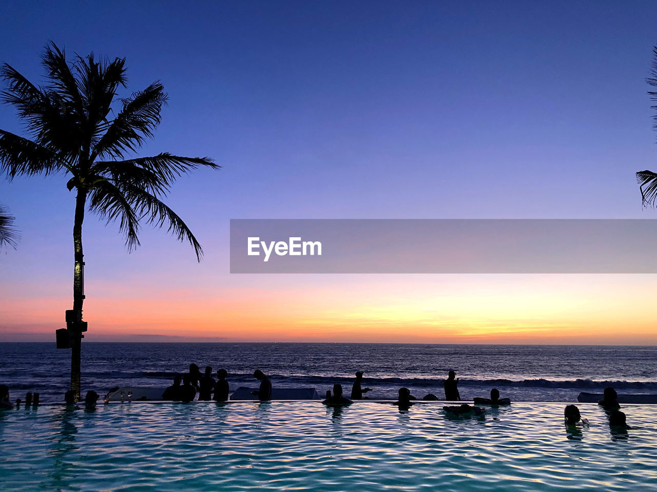 SILHOUETTE PEOPLE ON SWIMMING POOL AGAINST SKY AT SUNSET