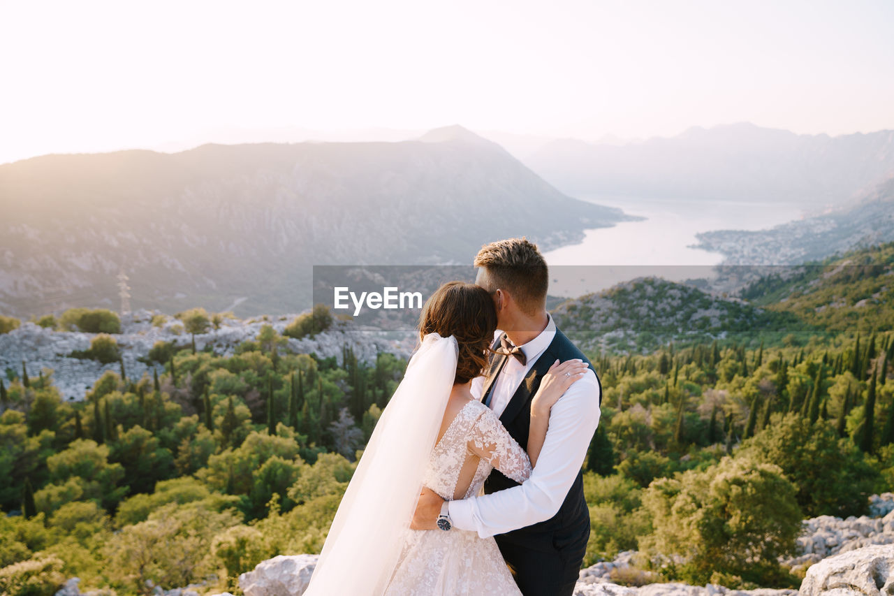 YOUNG COUPLE STANDING ON MOUNTAIN AGAINST MOUNTAINS