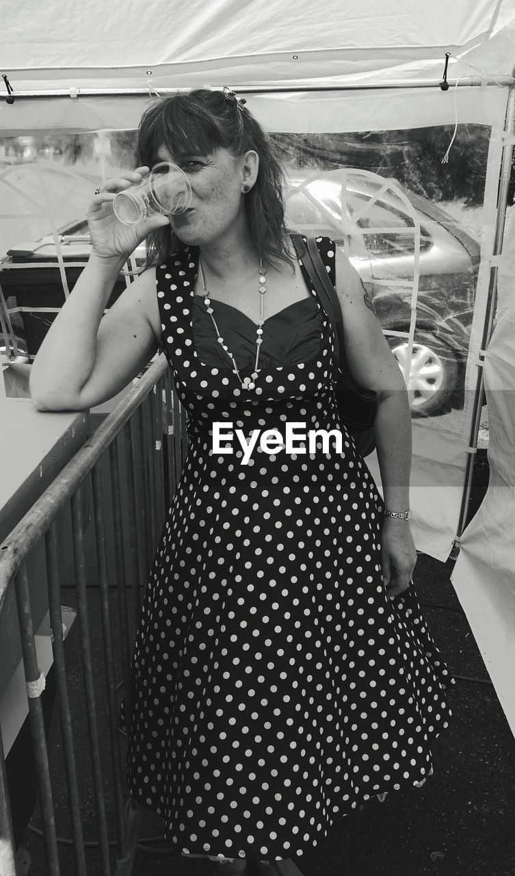 Portrait of woman drinking while standing by railing