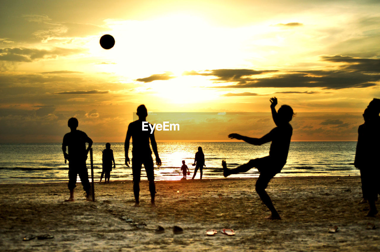 Silhouette people playing soccer at beach during sunset