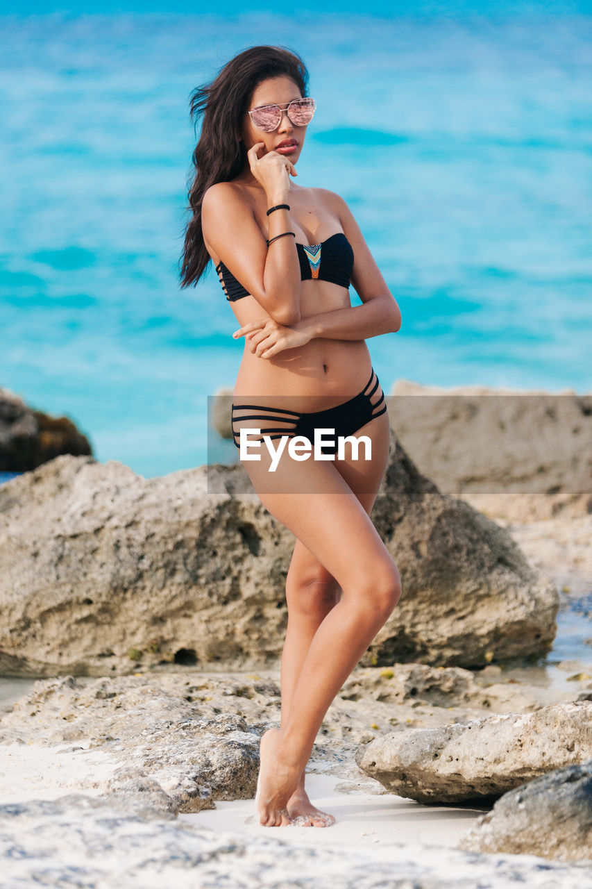 Woman in bikini and sunglasses standing at beach