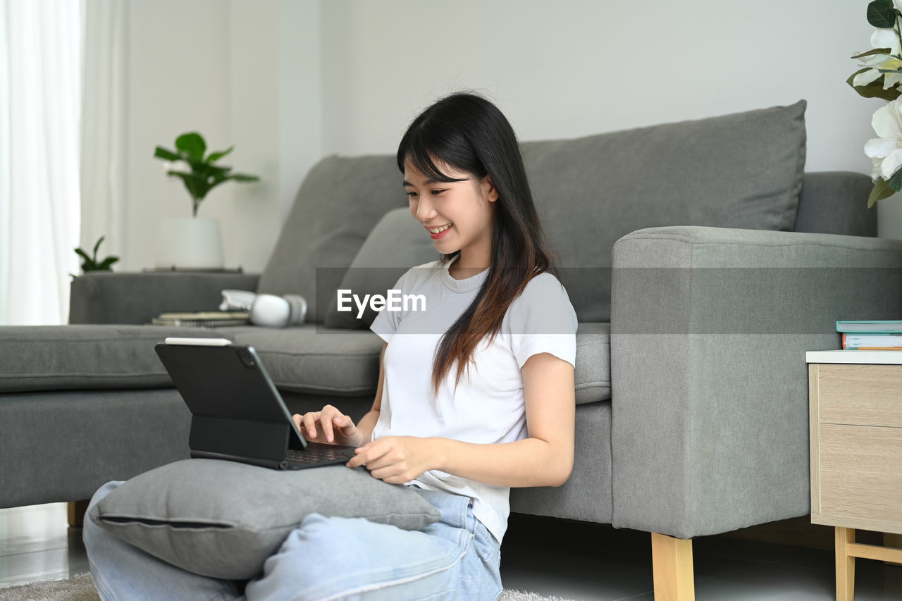 young woman using digital tablet while sitting on sofa at home