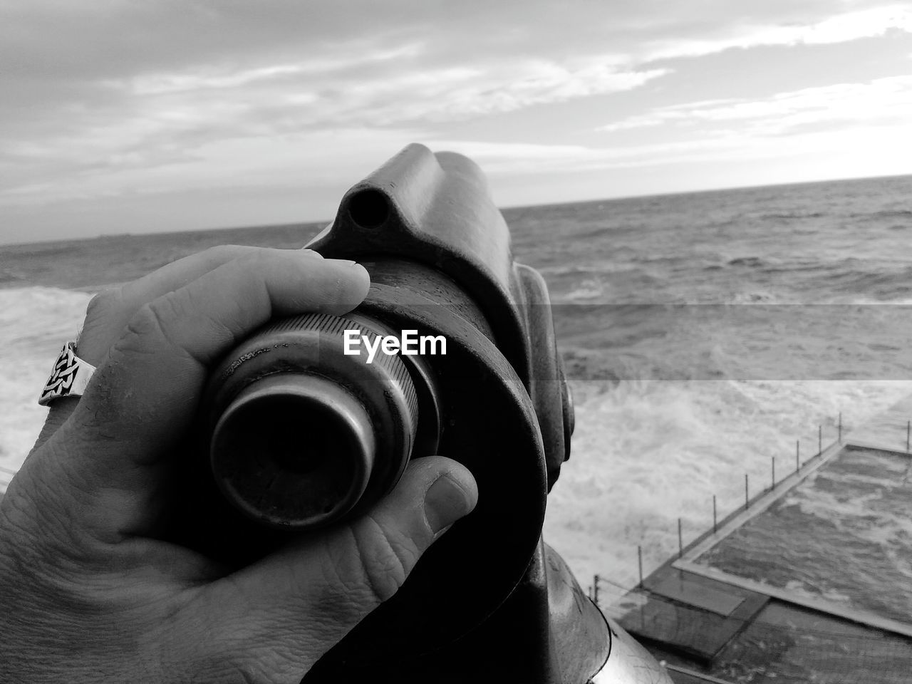 Cropped hand holding coin-operated binoculars against sky