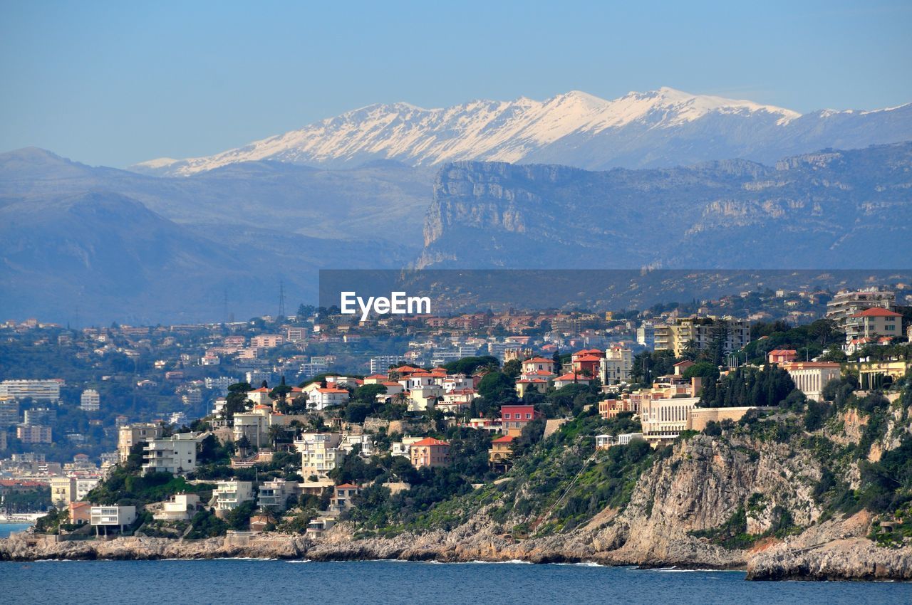 View of city by sea and mountains against sky