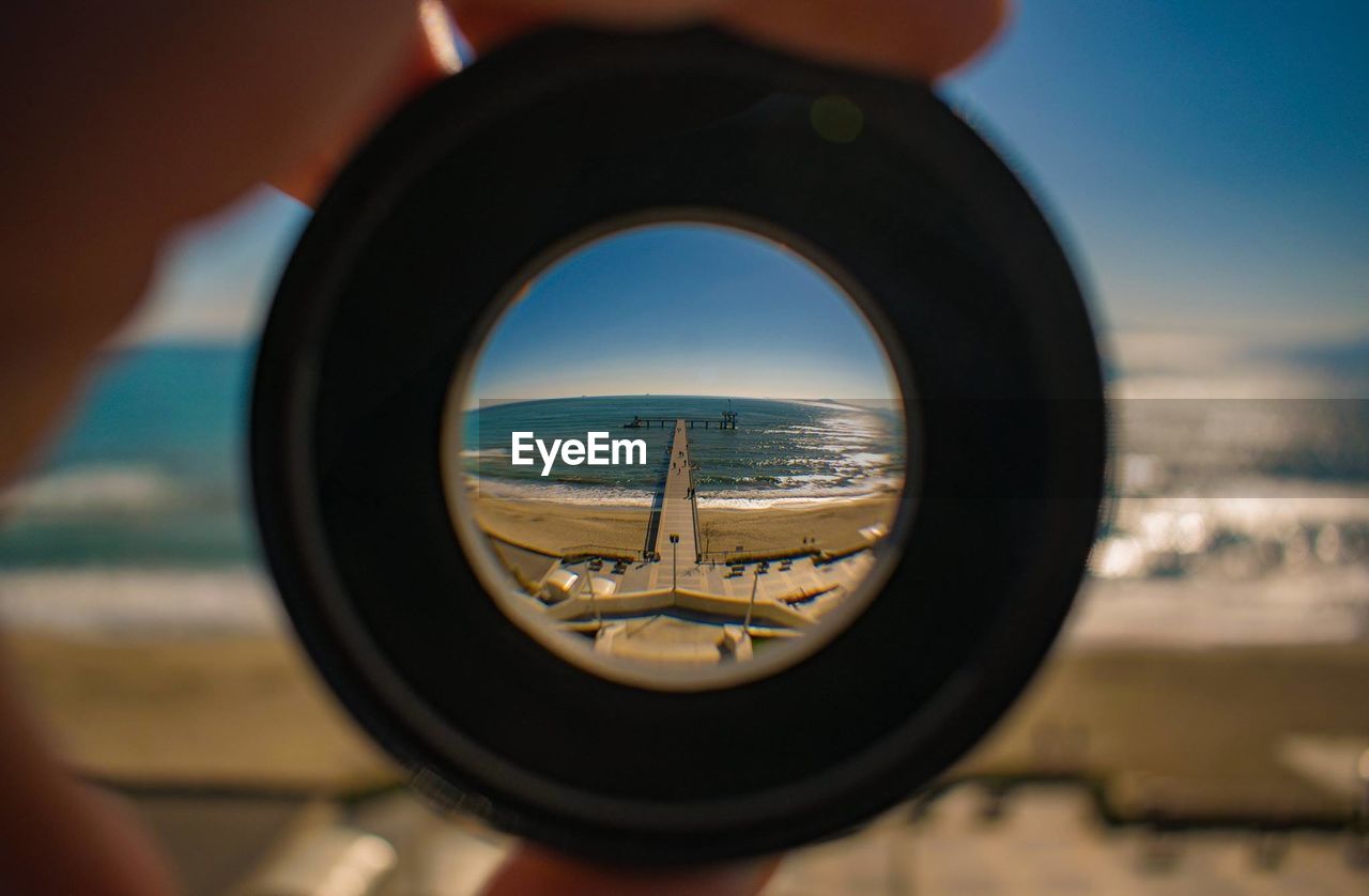 Cropped hand holding lens against pier