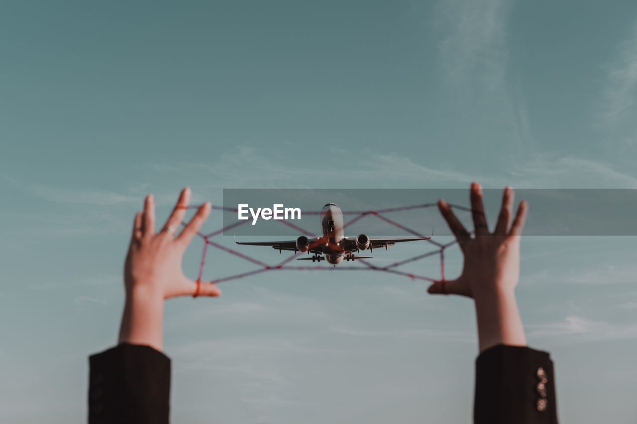 Cropped hands holding string against airplane flying in sky