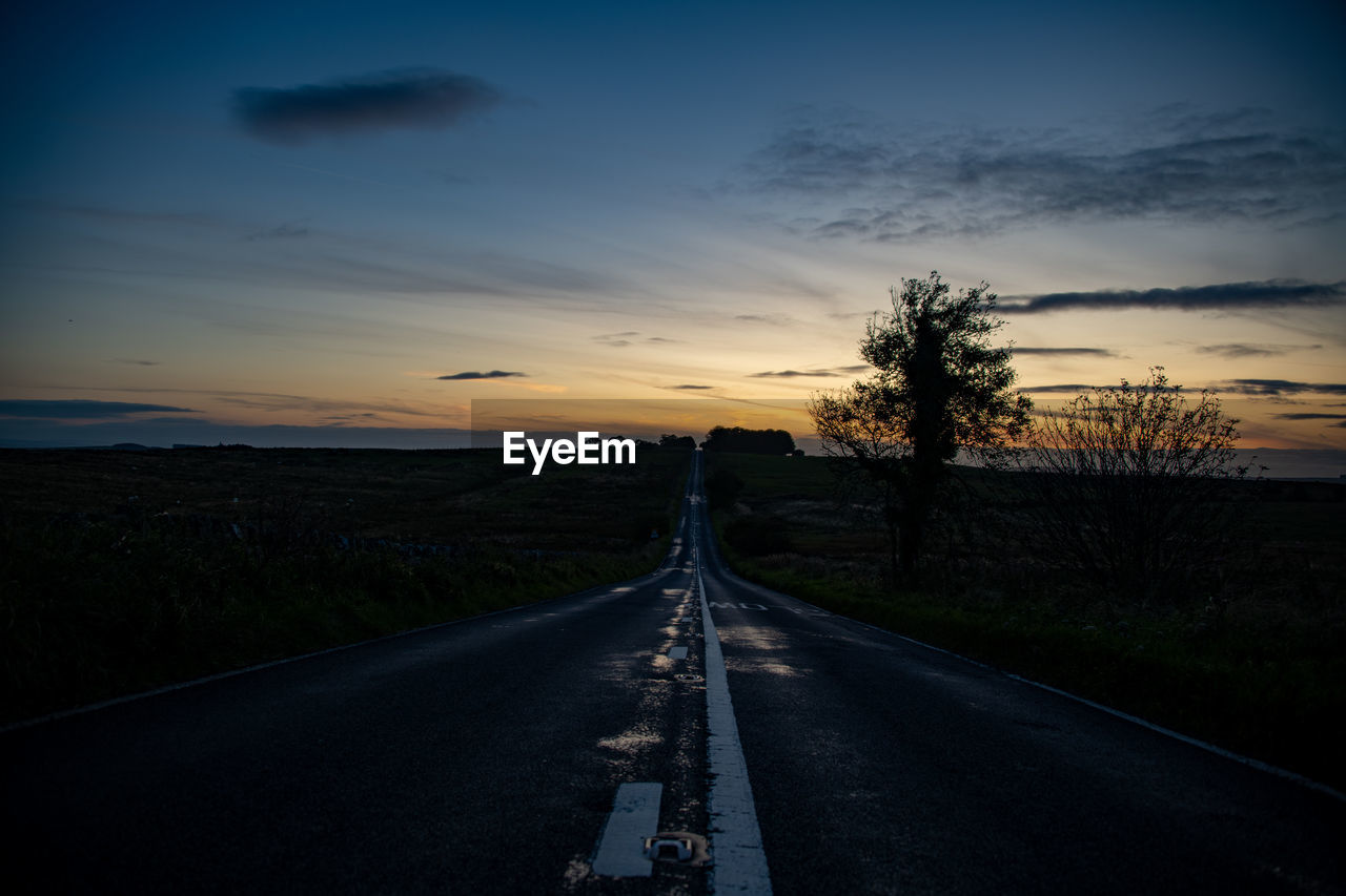 Empty road along landscape at sunset