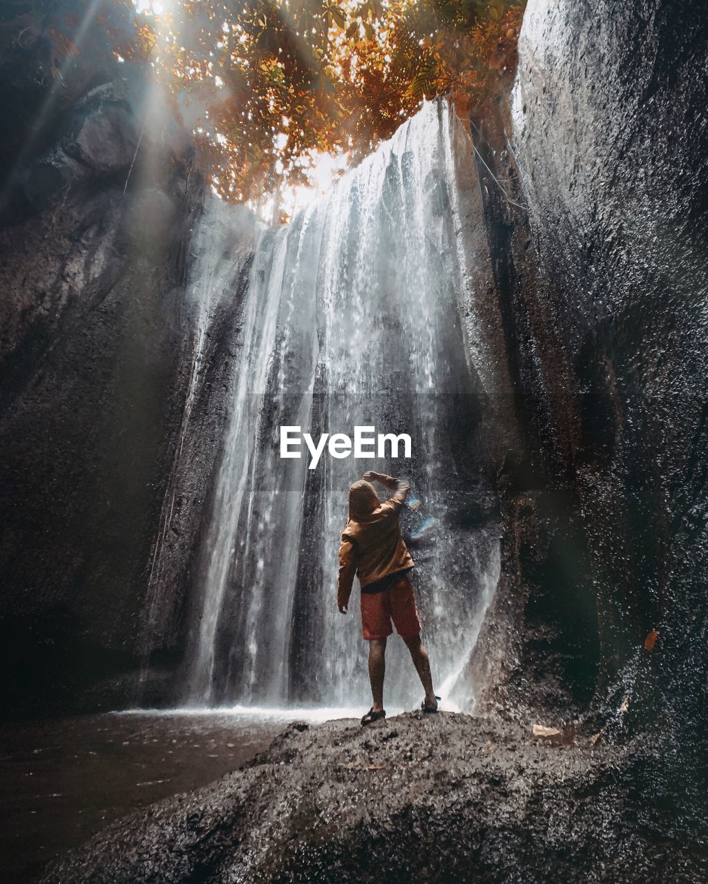 Rear view of man standing on rock against waterfall