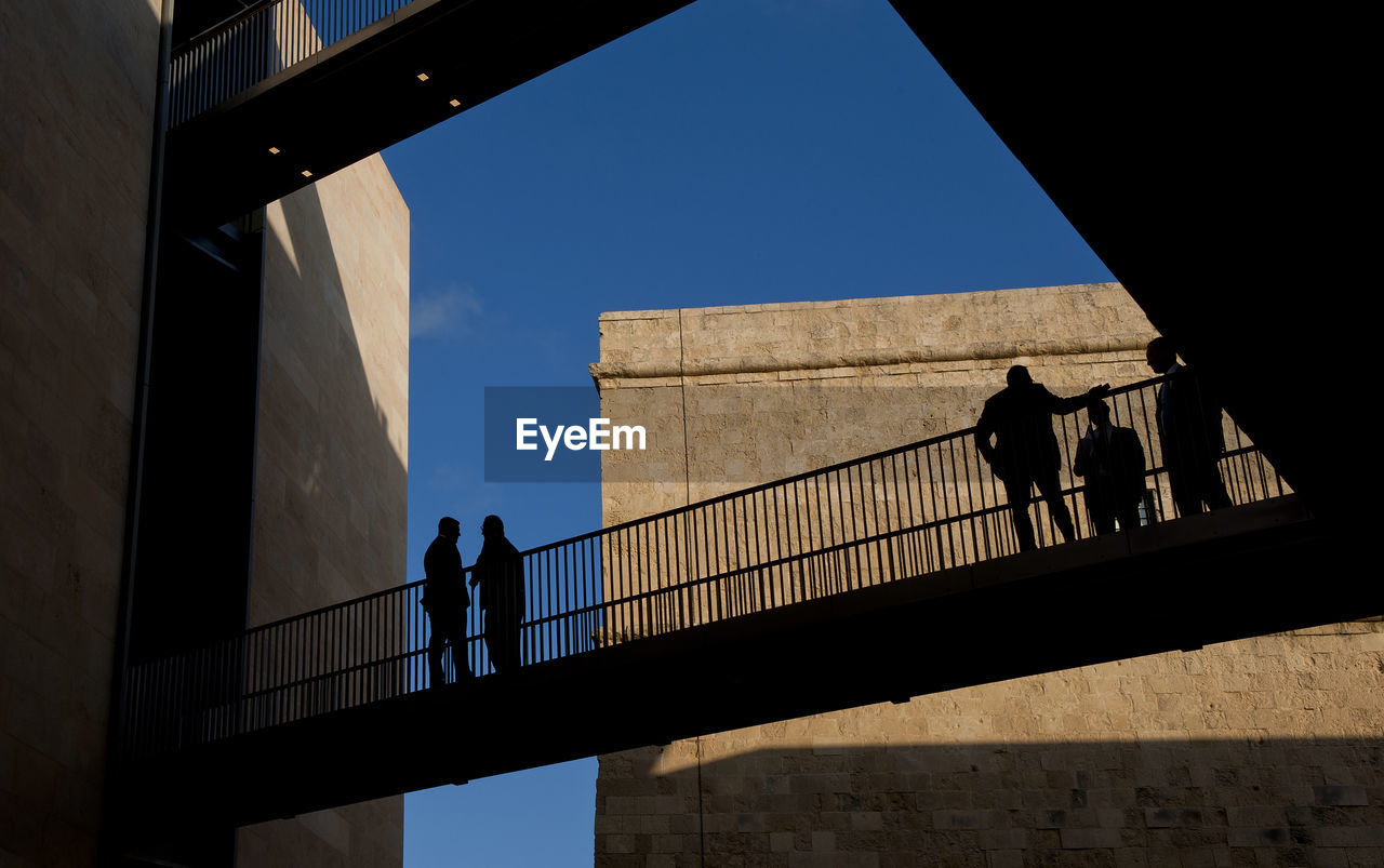 Low angle view of silhouette people walking on bridge against sky