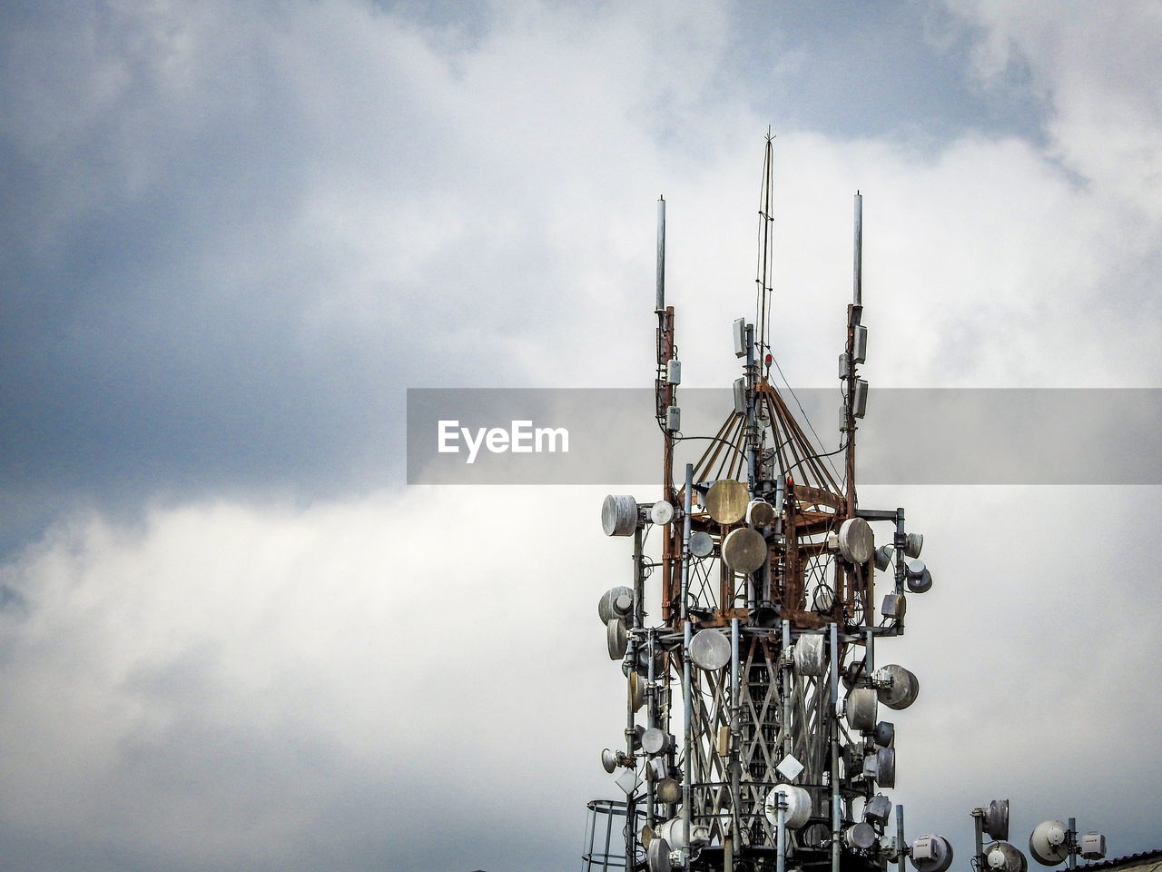 Close-up of communications tower against cloudy sky in city