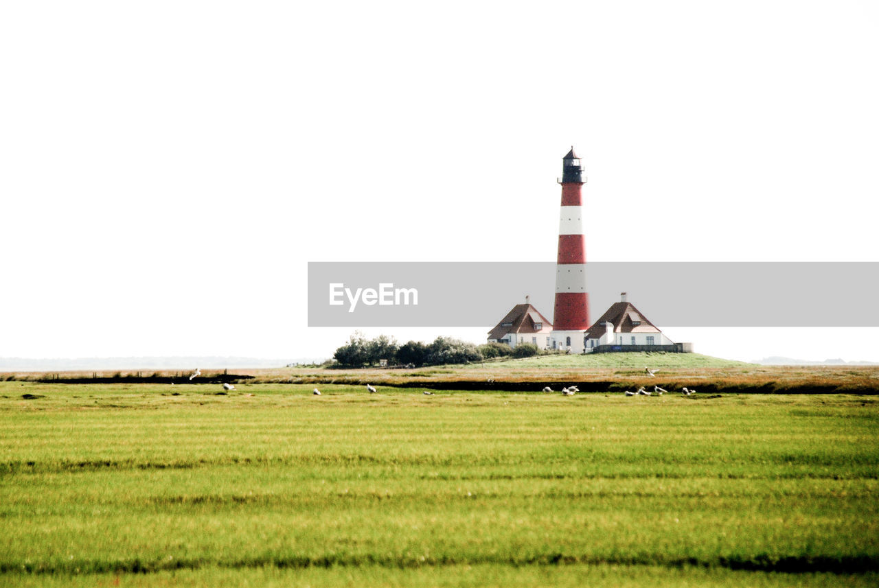 LIGHTHOUSE ON GRASSY FIELD AGAINST SKY