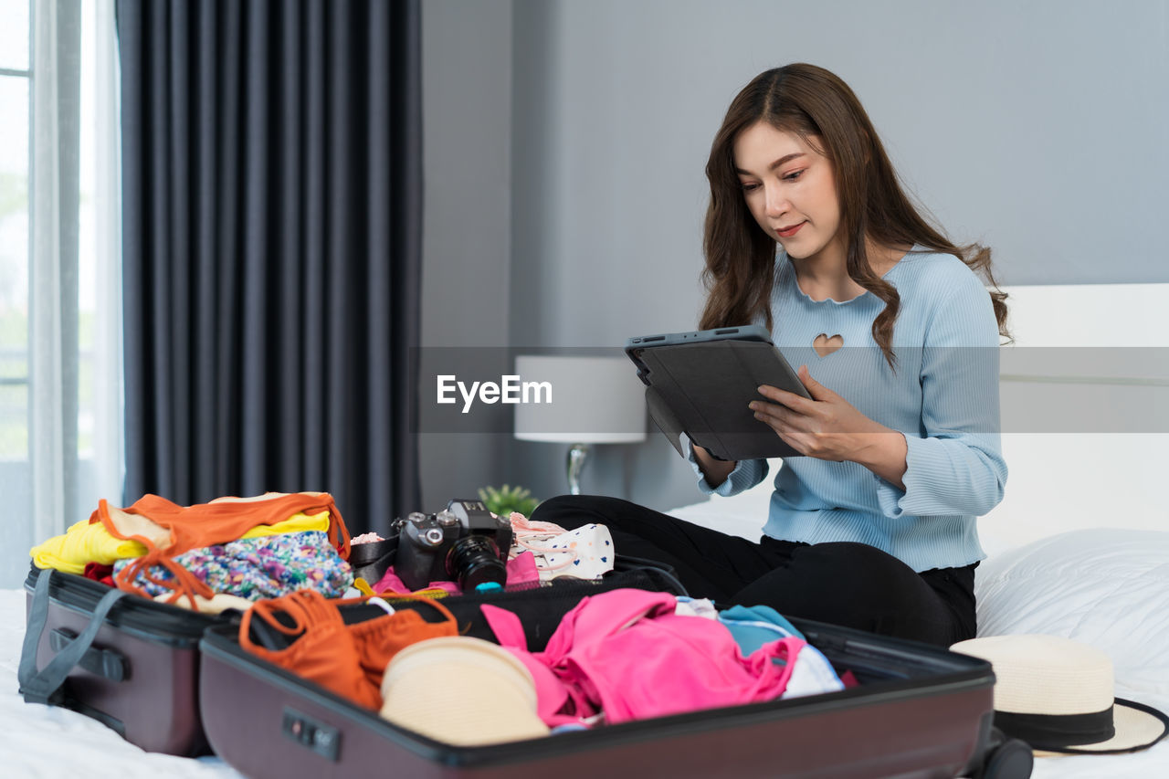 portrait of young woman using digital tablet while sitting on bed at home