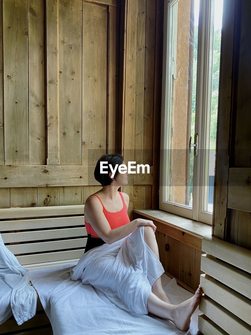 Side view of woman wearing a ba5ing suit sitting on wooden sit inside a sauna