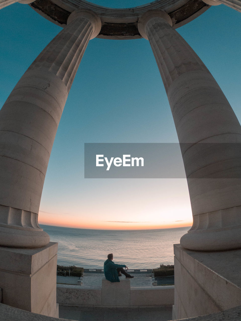 Man sitting at beach seen through gate