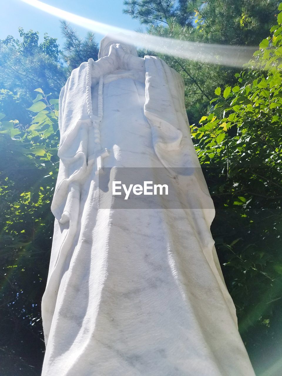 LOW ANGLE VIEW OF STATUE HANGING AGAINST TREES