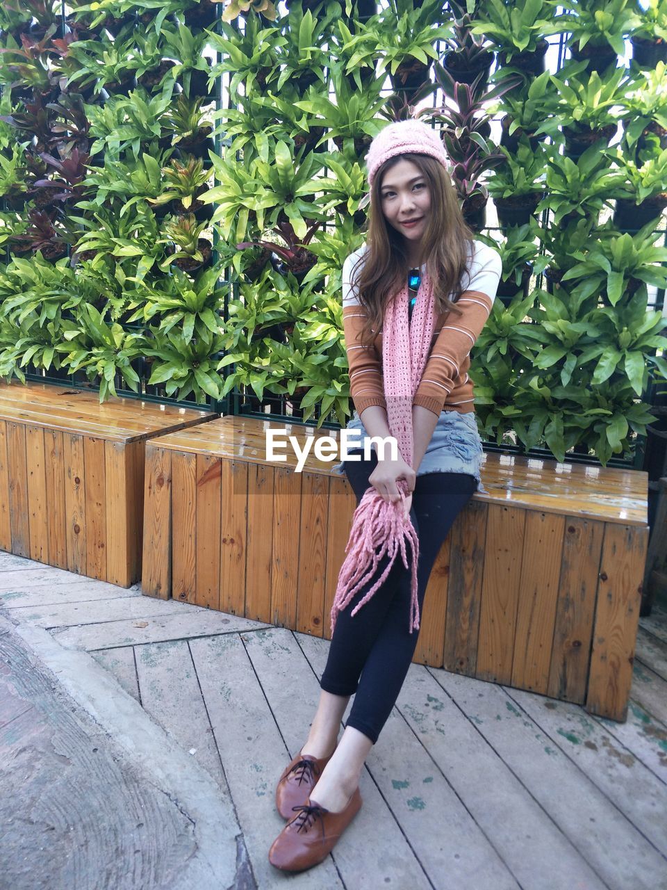 Full length portrait of smiling woman sitting against plants