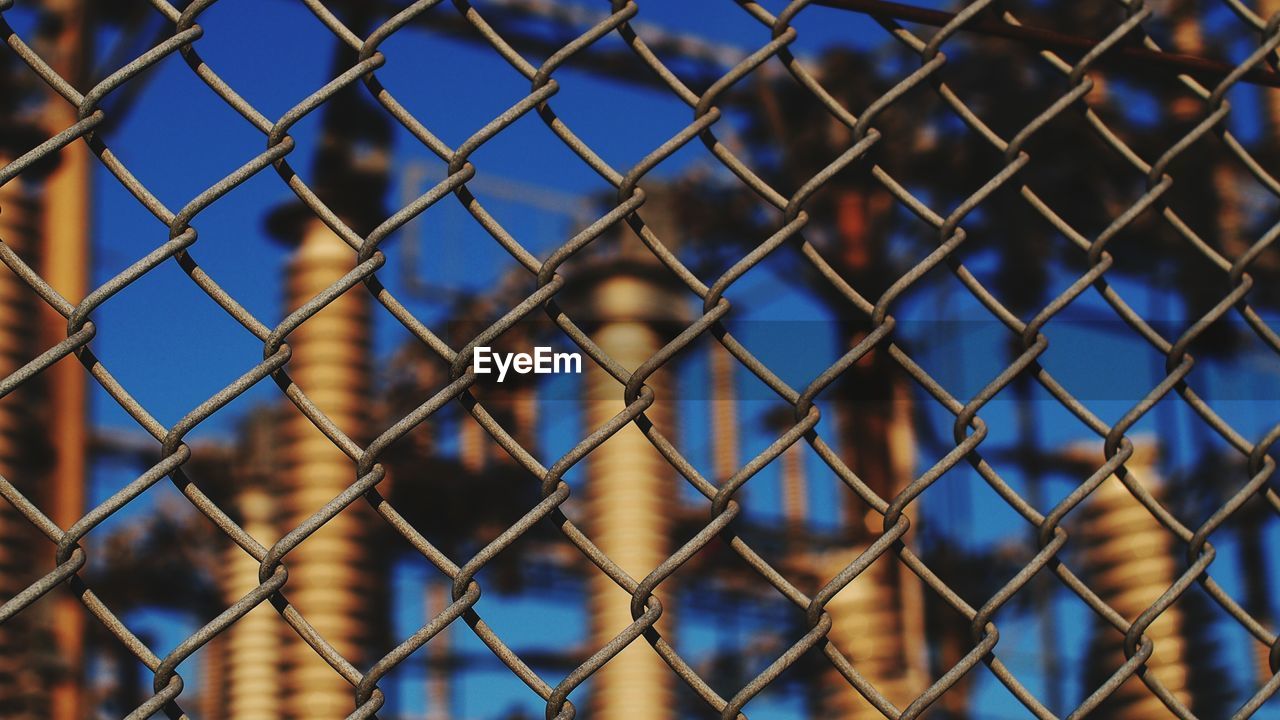 Low angle view of power station seen from chainlink fence