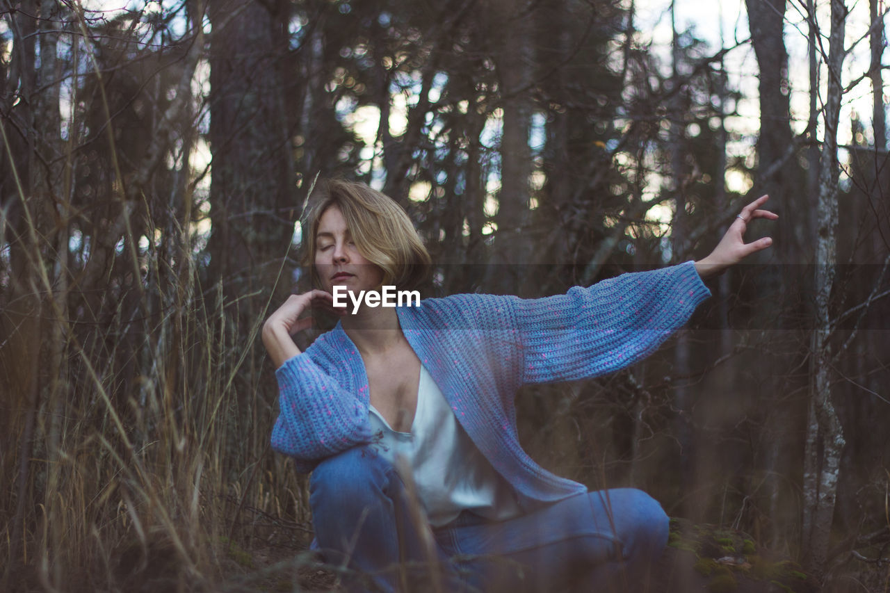 Young woman with eyes closed dancing against trees in forest