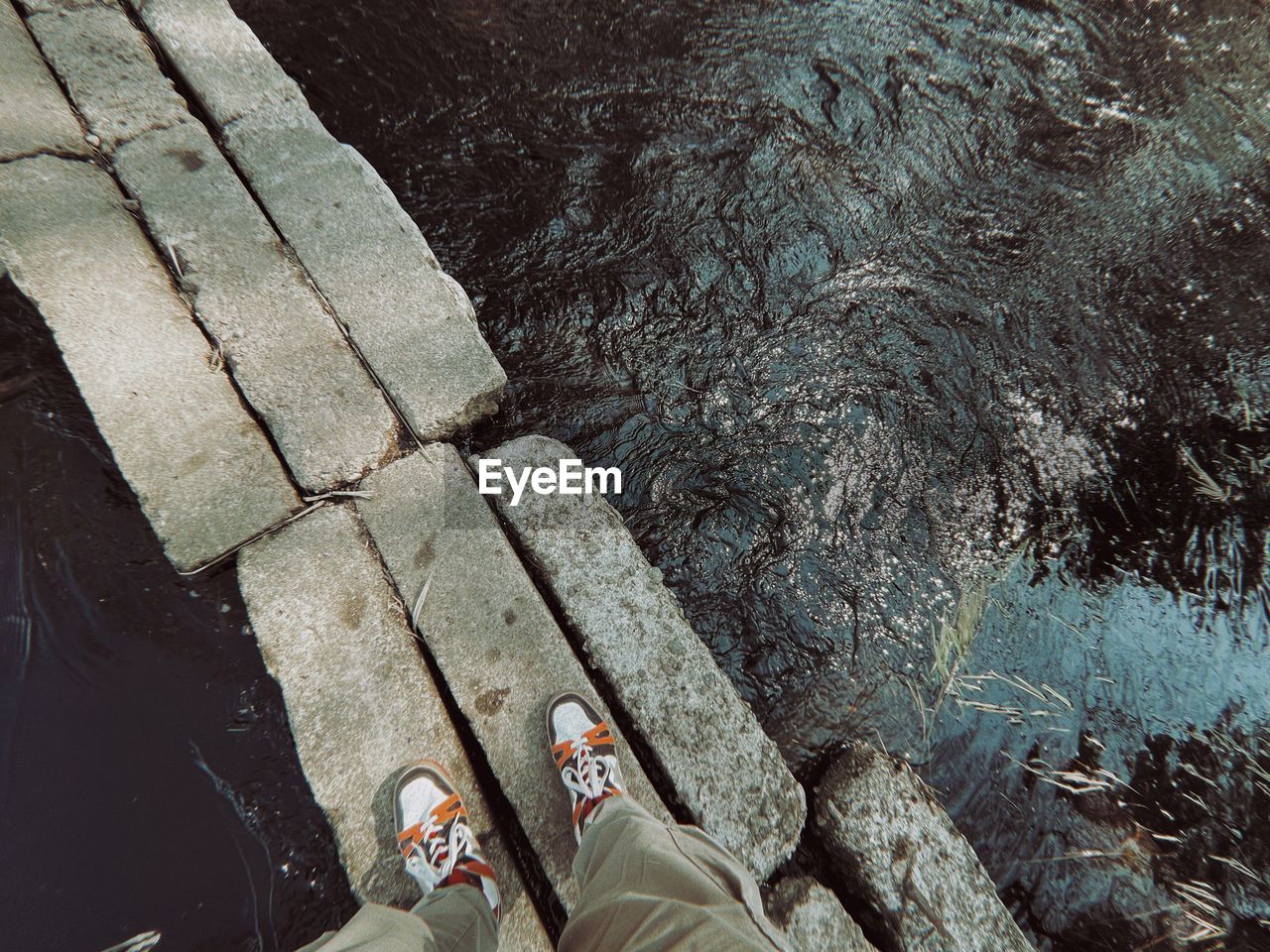 low section, human leg, shoe, personal perspective, high angle view, one person, water, lifestyles, standing, day, nature, leisure activity, rock, human foot, directly above, outdoors, limb, human limb, wall, men, footpath, wet, reflection, adult, women, soil