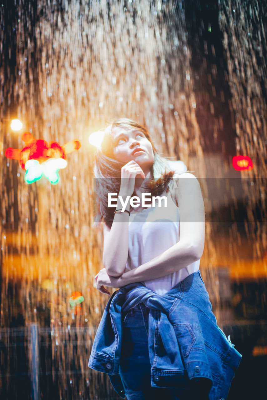 Woman looking away against illuminated waterfall at night