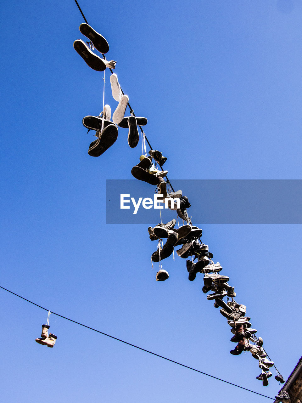 Low angle view of shoes hanging on cables against clear blue sky during sunny day