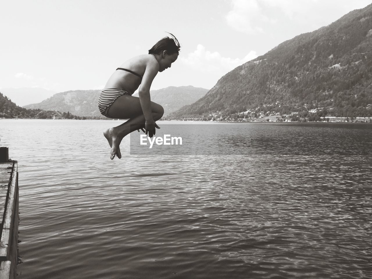 Full length of girl jumping in lake against sky
