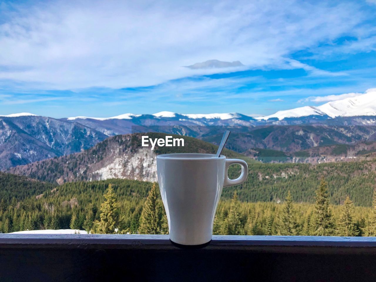 White cup placed on wooden railing on the balcony with view of snowcapped mountains