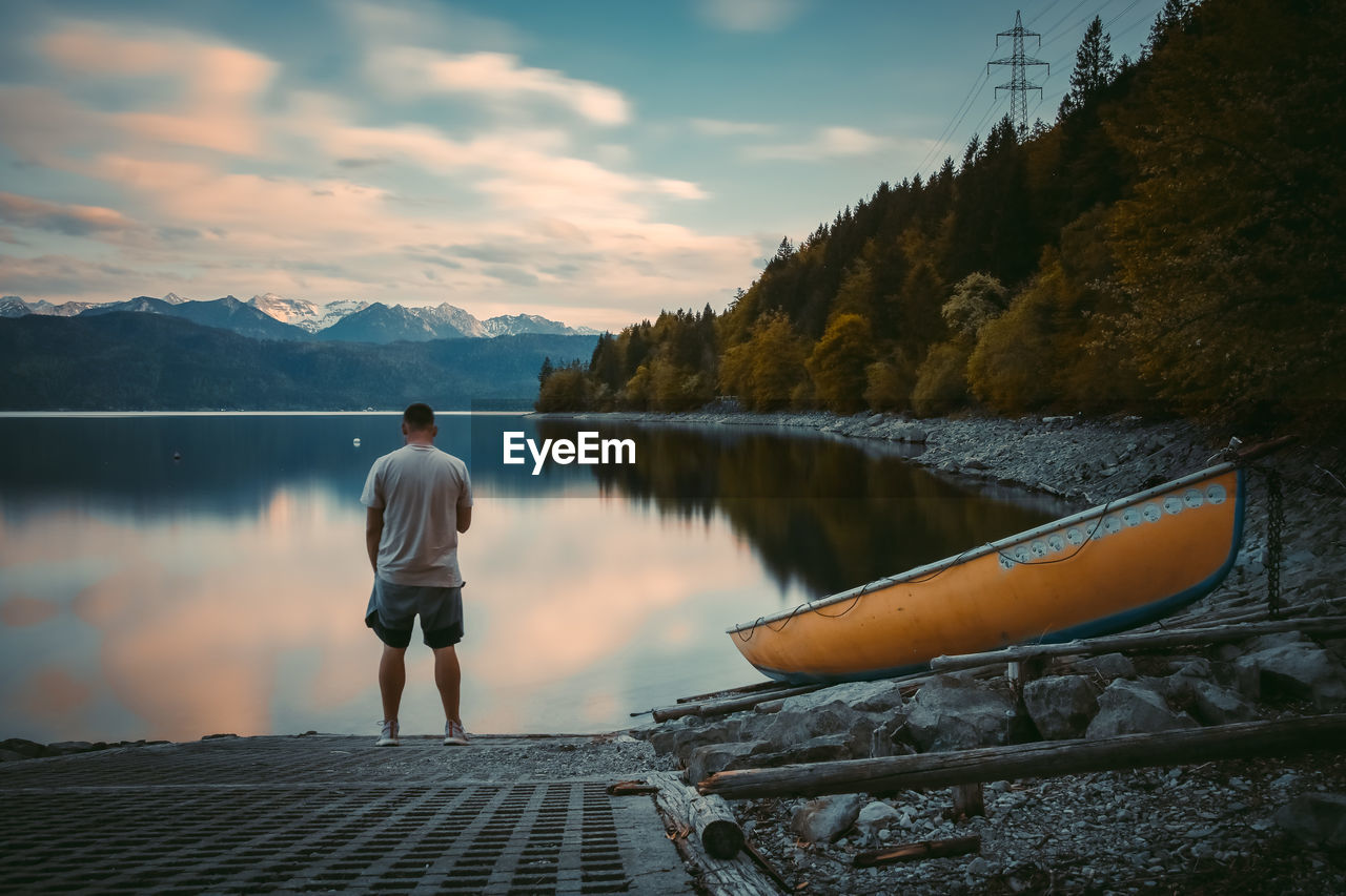 Rear view of man standing on lake against sky