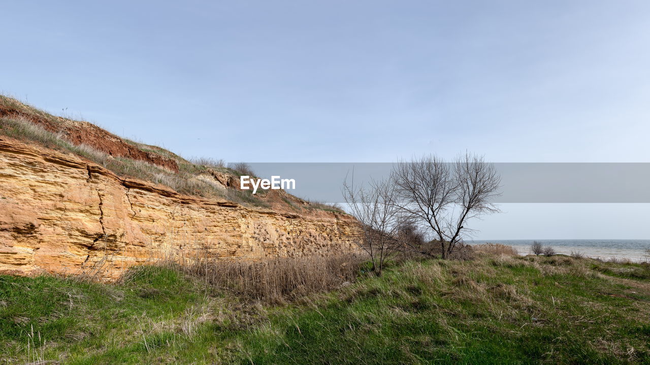 sky, plant, land, nature, grass, scenics - nature, cliff, landscape, hill, rock, environment, terrain, no people, beauty in nature, sea, non-urban scene, tranquility, water, tranquil scene, tree, coast, rural area, travel destinations, cloud, day, outdoors, travel, tourism, blue, clear sky, horizon, remote, geology