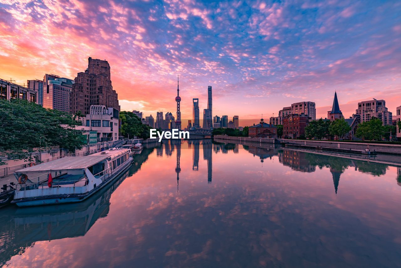 SCENIC VIEW OF LAKE BY BUILDINGS AGAINST SKY DURING SUNSET