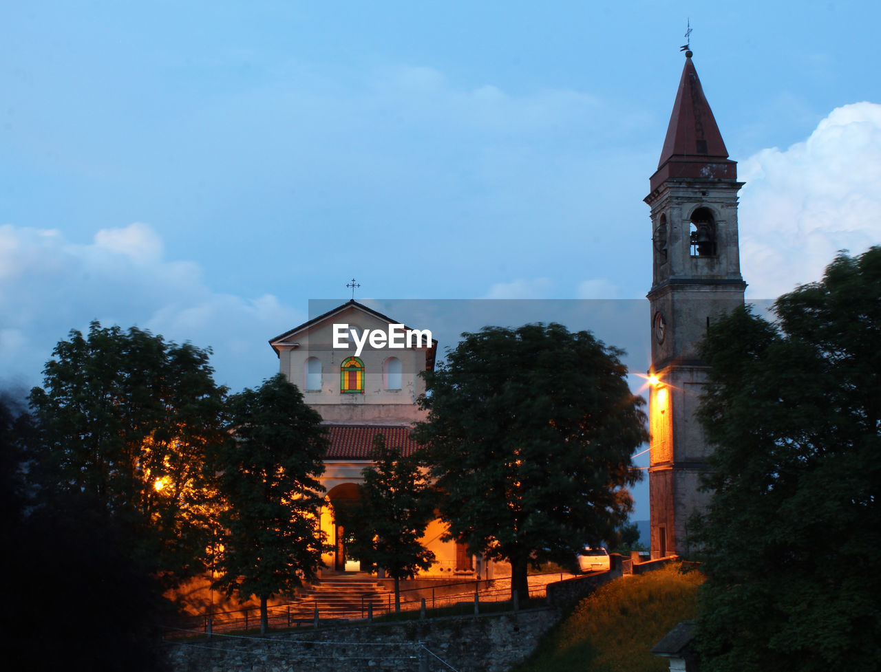 ILLUMINATED BUILDING BY TREES AGAINST SKY