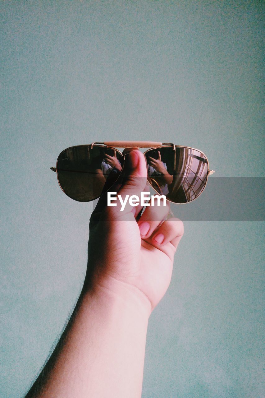 Close-up of hand holding sunglasses against wall