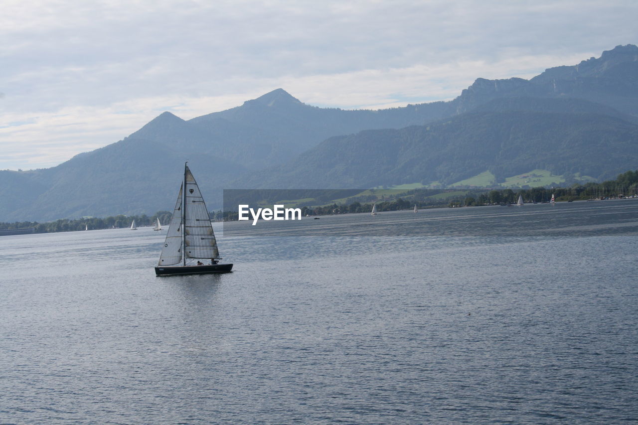 SAILBOAT ON CALM SEA AGAINST MOUNTAINS