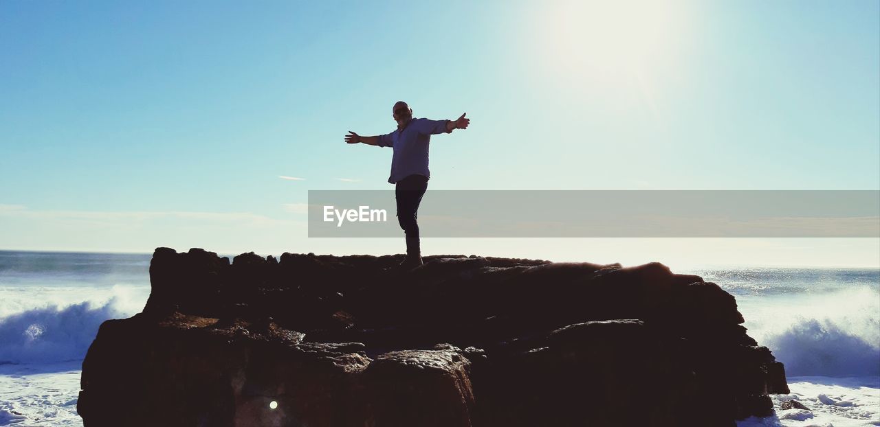 Man standing on rock by sea against sky