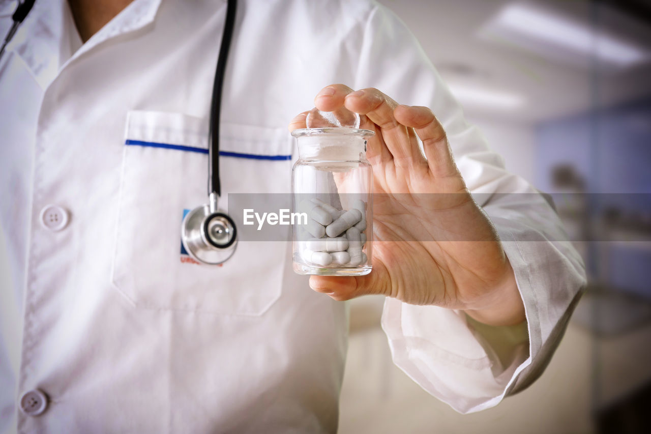 Midsection of doctor holding pills in container