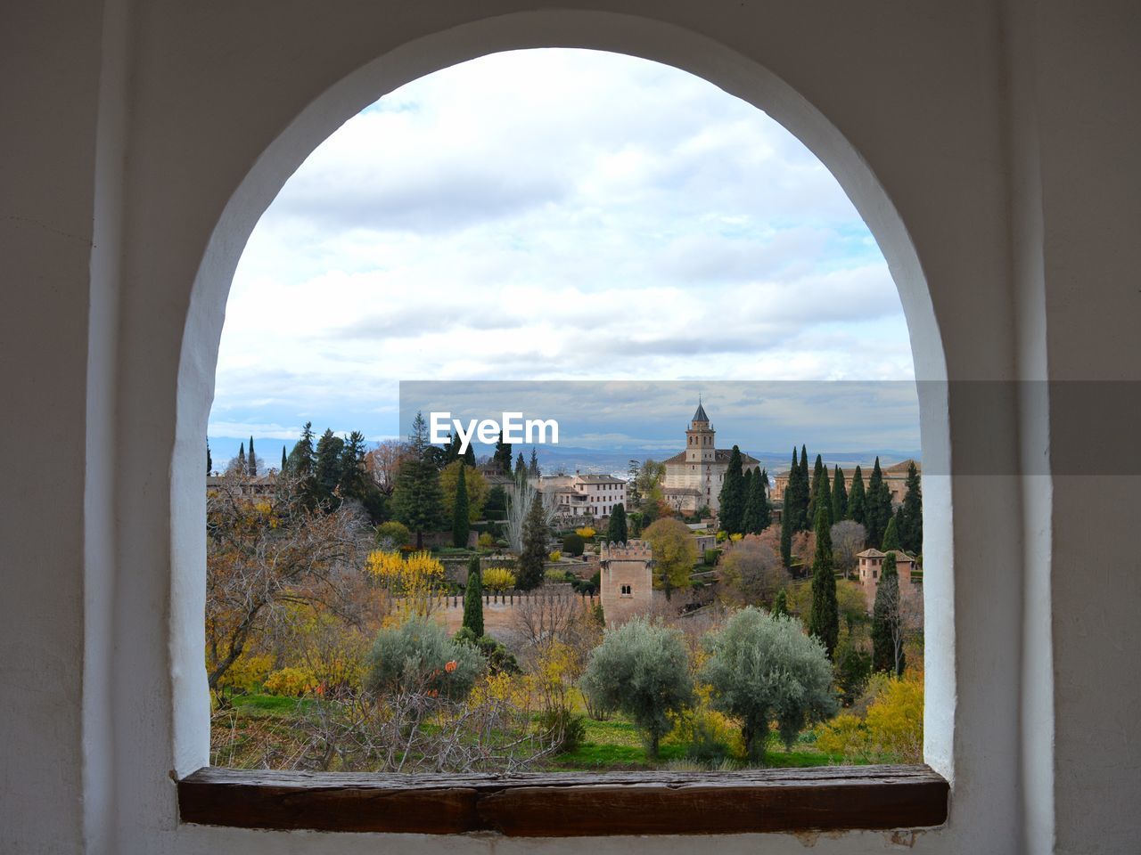 Trees and buildings against sky seen through window. view to sacromonte from alhambra palace granada