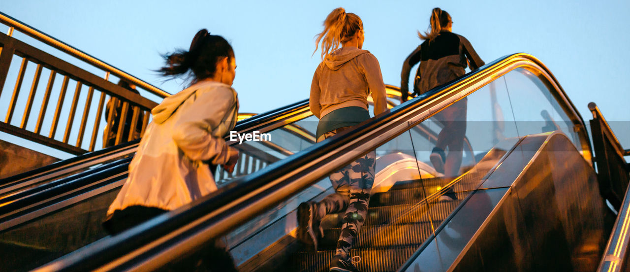 Women friends training running up escalator in city on sunset