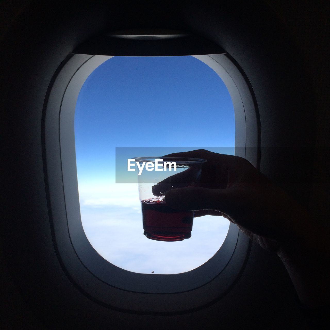Cropped hand holding drinking glass by window while traveling in airplane