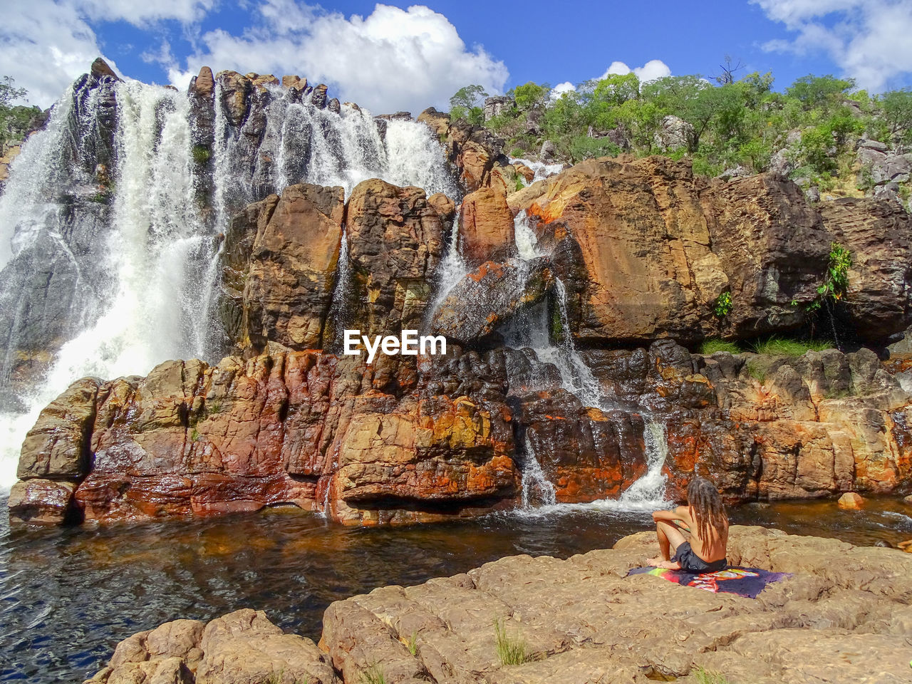 Man sitting on rock formations against waterfall